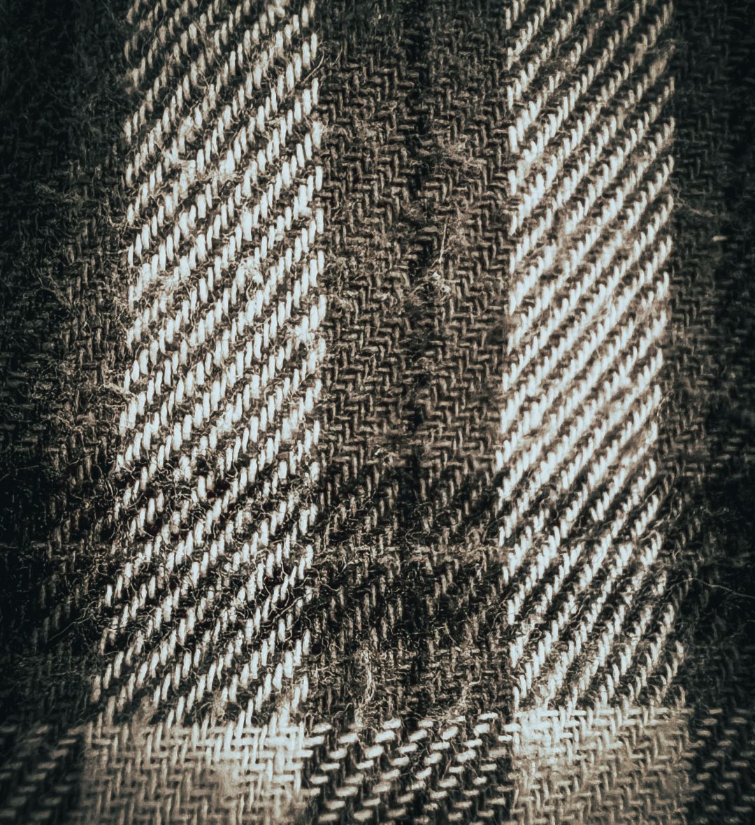 A close-up of woven wool fabric with diagonal white and black striped patterns, photographed with an ultra-wide macro lens that emphasizes the texture and weave of the material.